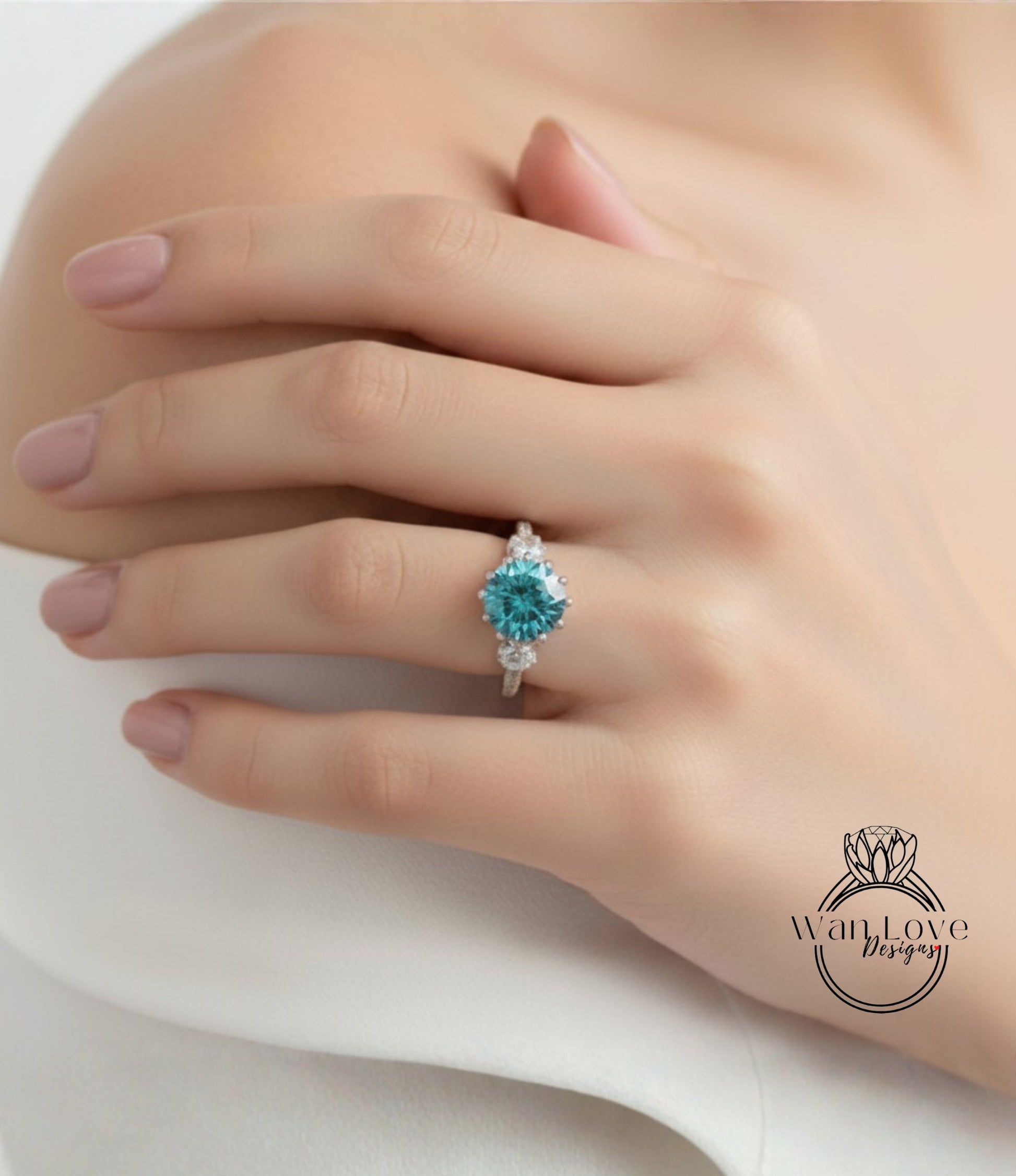 A close-up of a hand wearing a ring with a blue gemstone, resting on a white surface.