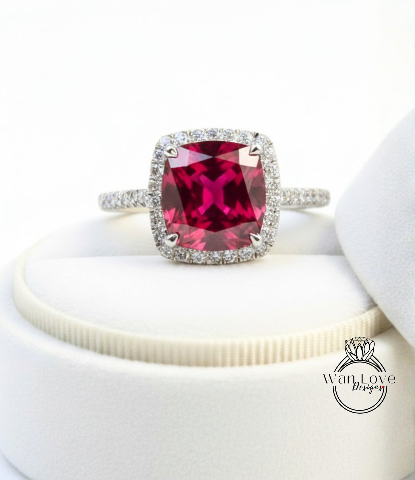 A stunning ring featuring a large, deep red gemstone set in a halo of smaller diamonds, placed on a white surface.