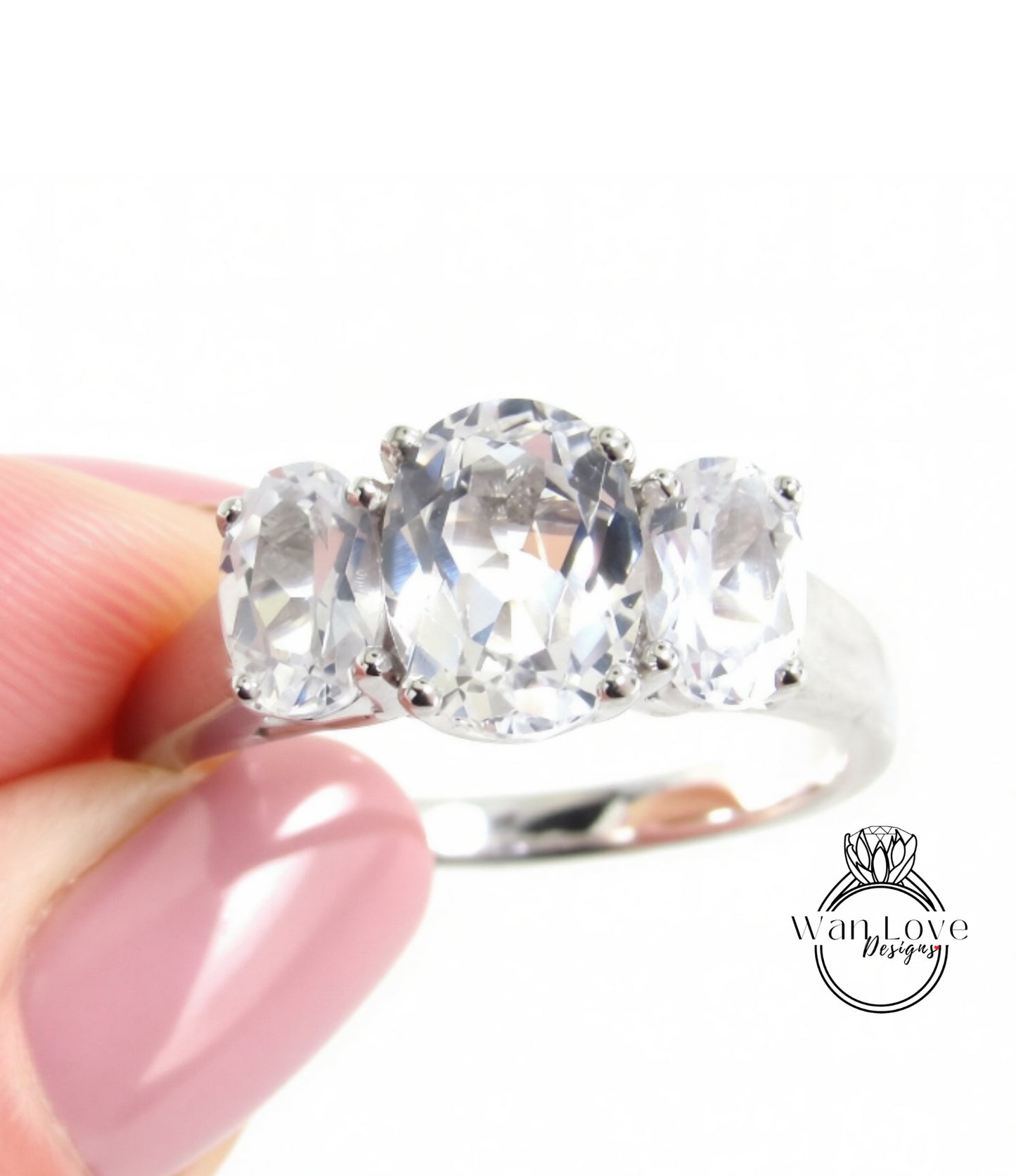 A close-up of a person's hand holding a silver ring with three large, clear gemstones.