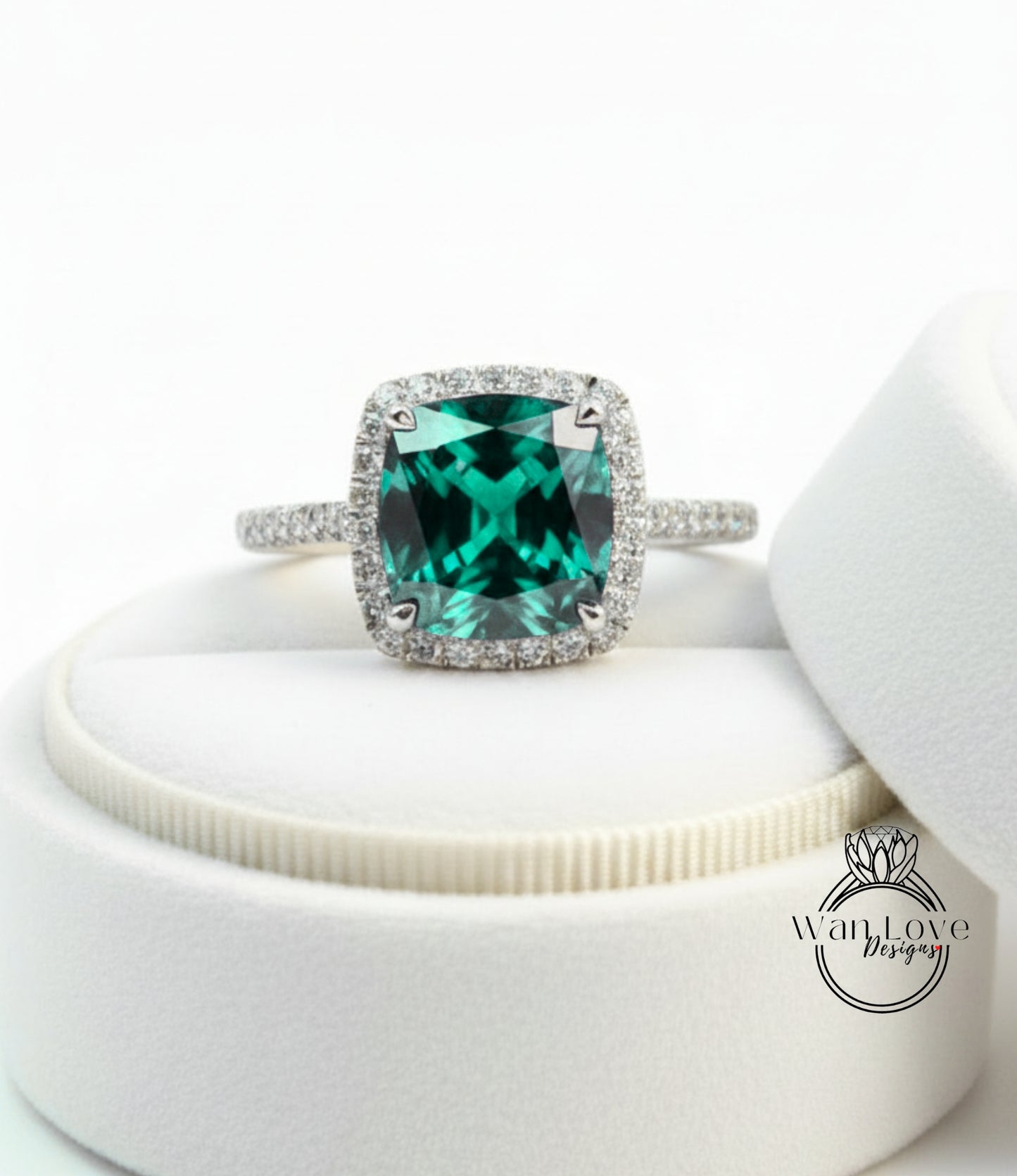 A diamond ring with a large, green gemstone set in a halo of smaller diamonds, displayed on a white jewelry box.
