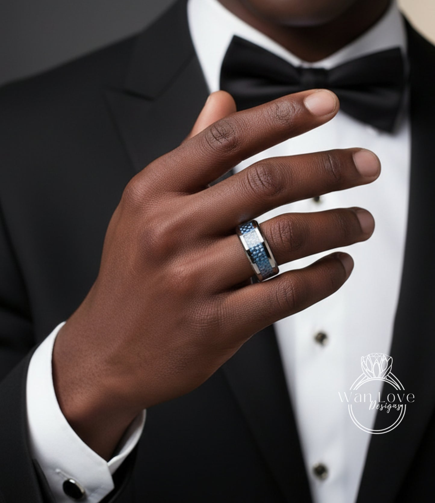 A close-up of a man's hand wearing a ring, with a black suit and bow tie visible.