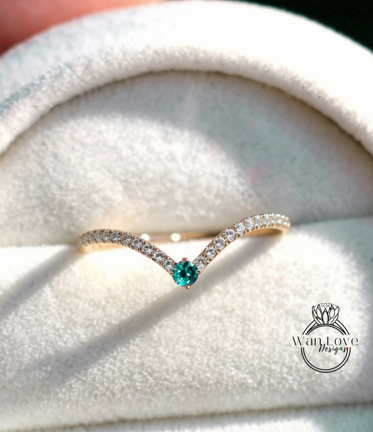 A gold ring with a green gemstone, placed on a white velvet background.
