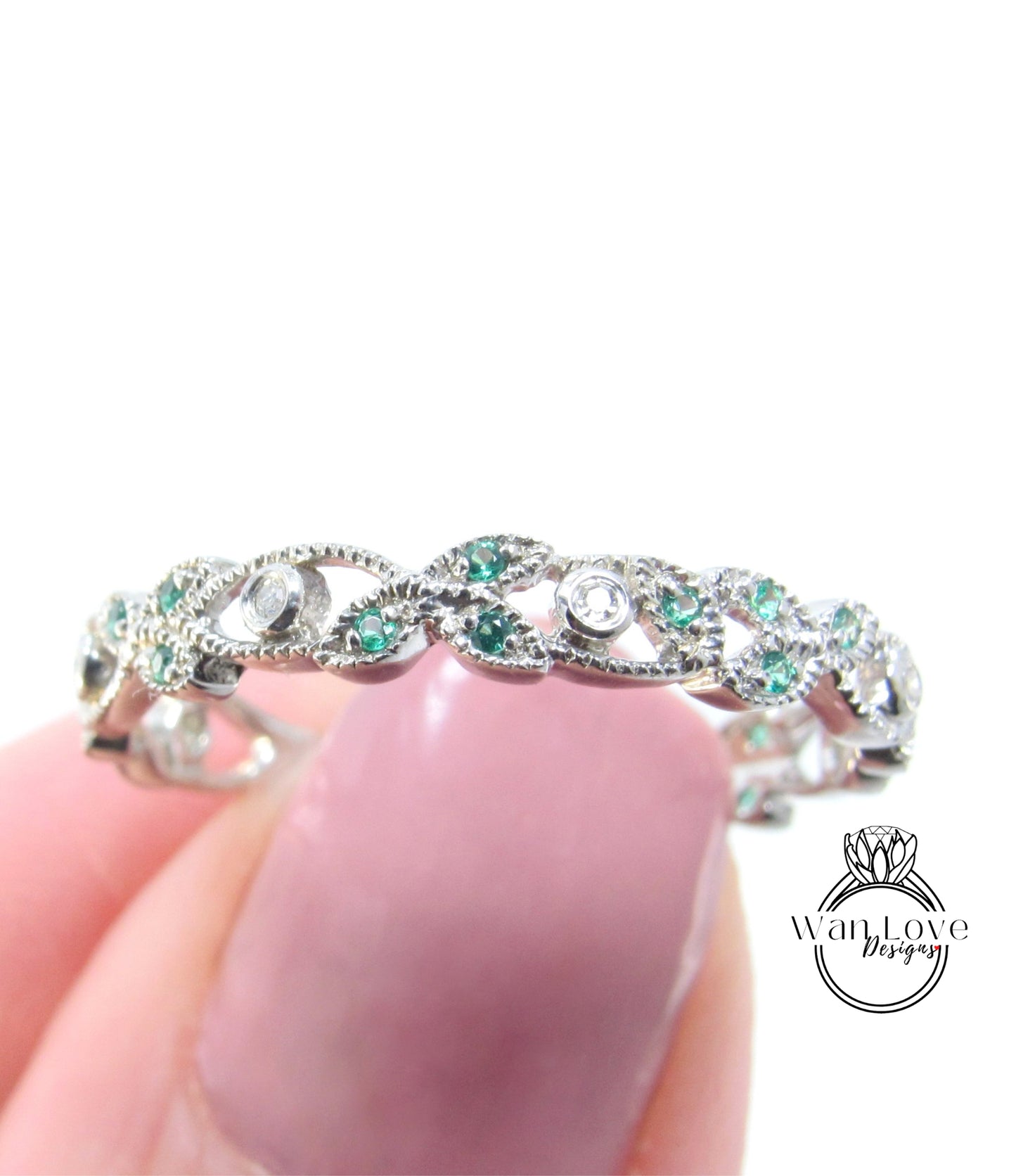 A close-up image of a person's hand holding a silver ring adorned with green and white gemstones.