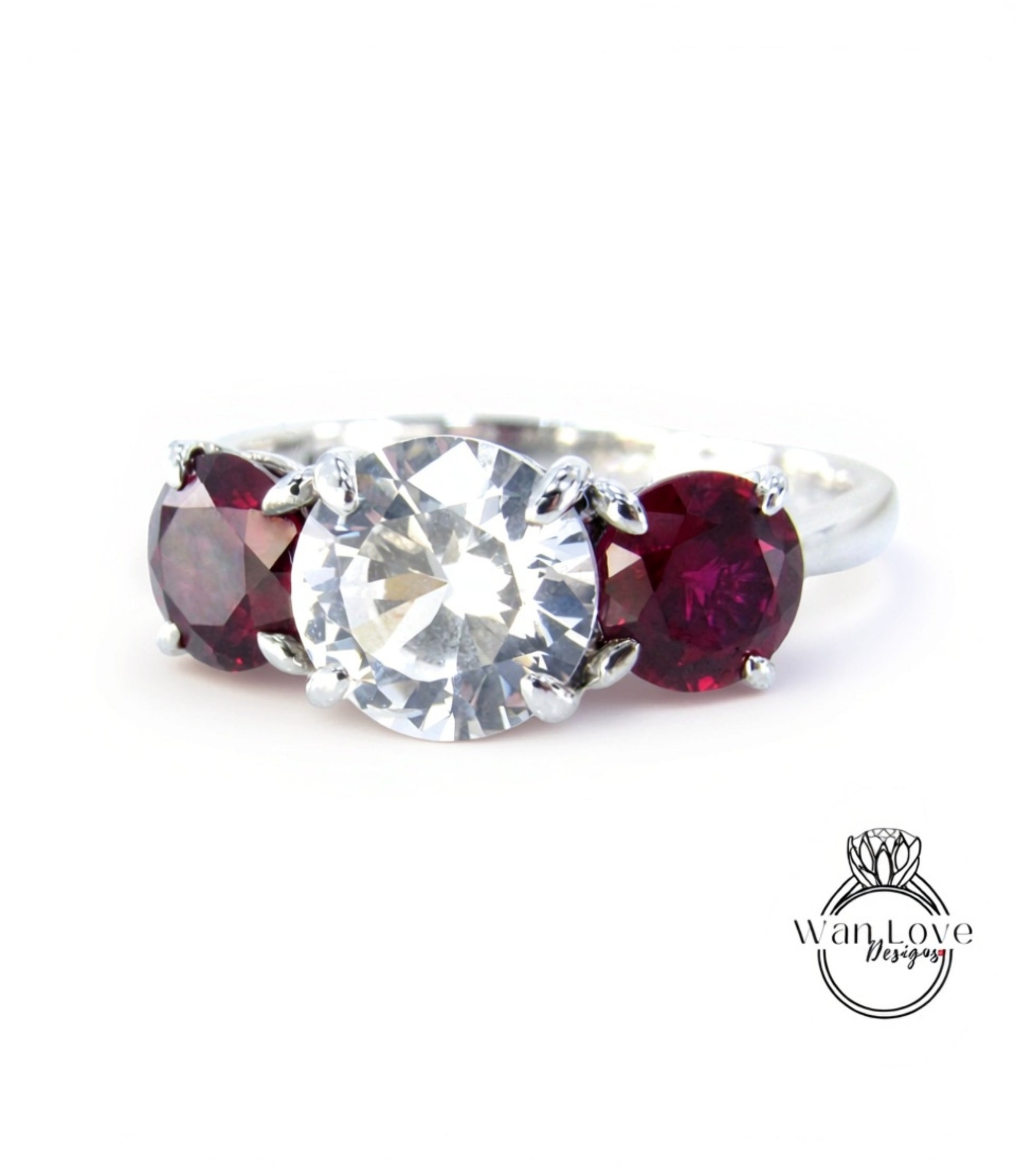 A close-up image of a ring with a large, clear gemstone surrounded by two smaller, deep red gemstones.