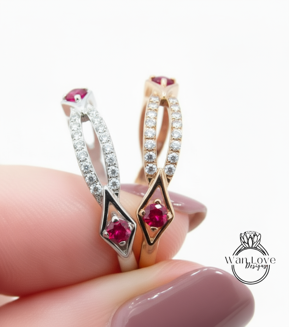 A close-up of a person's hand holding a ring with two gemstone designs, one silver and one gold, with the gemstones being red.