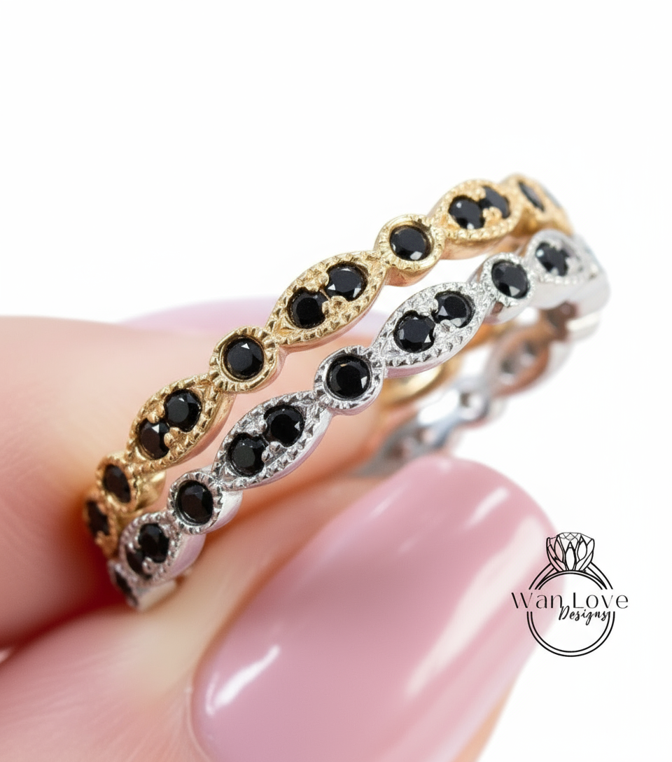 A close-up image of a person's hand wearing a ring with a row of black gemstones, including diamonds, on a pink background.