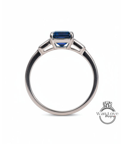 A silver engagement ring with a blue gemstone, possibly a sapphire, set in a three-pronged design.