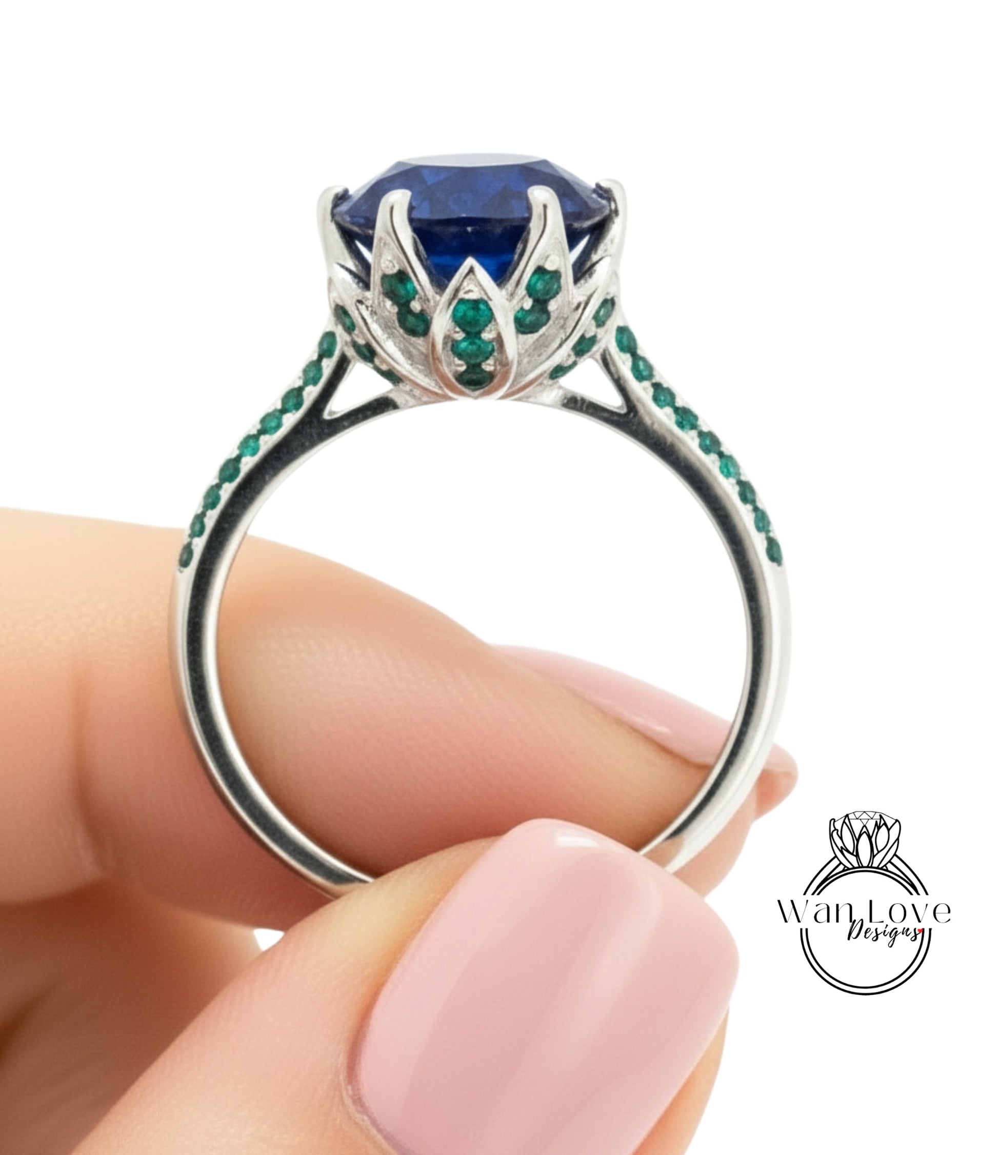 A hand holding a silver ring with a large blue gemstone and green gemstones.