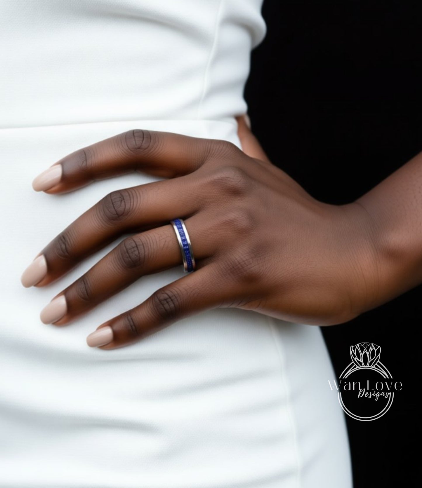 A close-up of a person's hand wearing a ring with a blue gemstone, resting on a white dress.