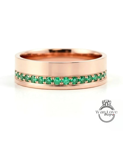 A rose gold band with a row of green gemstones set in it.