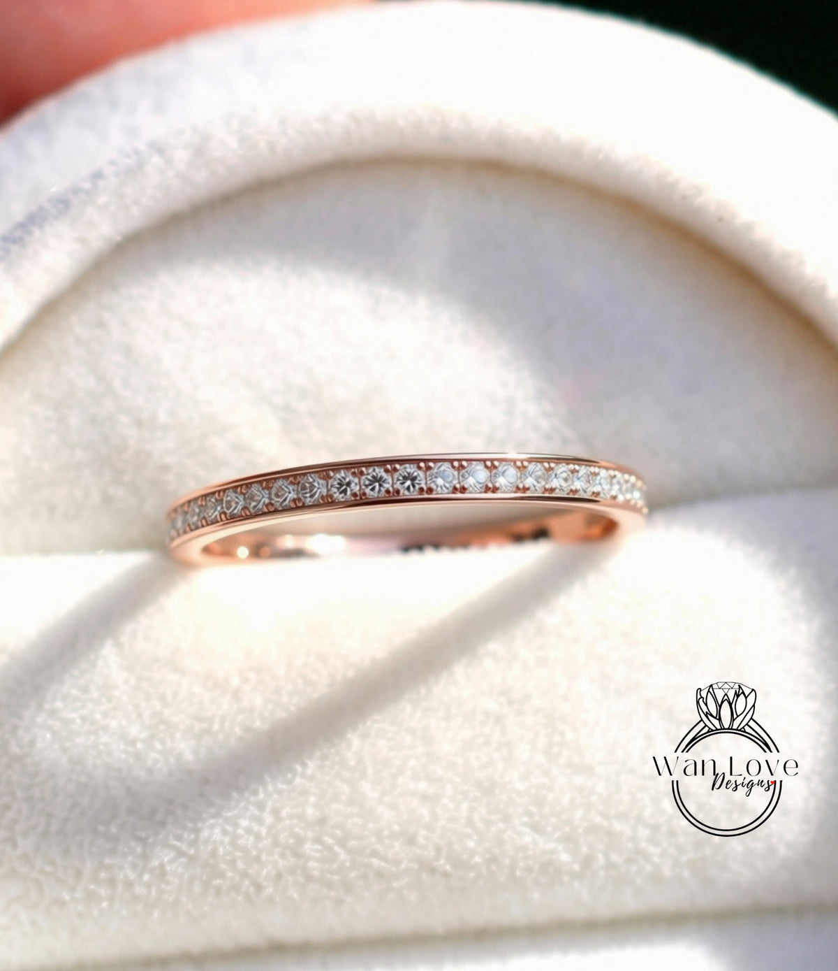 A rose gold band ring with a row of small diamonds set in it, displayed on a white velvet background.