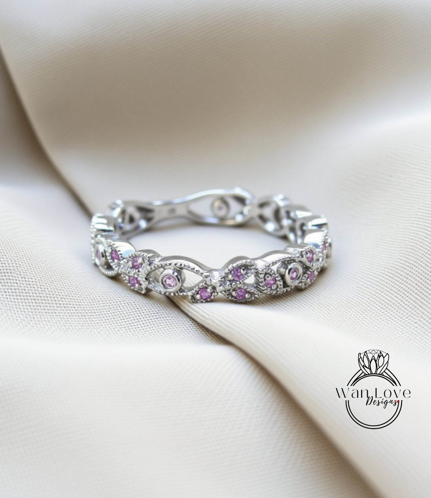 A silver ring with a floral design and small purple gemstones is displayed on a white fabric background.
