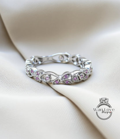 A silver ring with a floral design and small purple gemstones is displayed on a white fabric background.