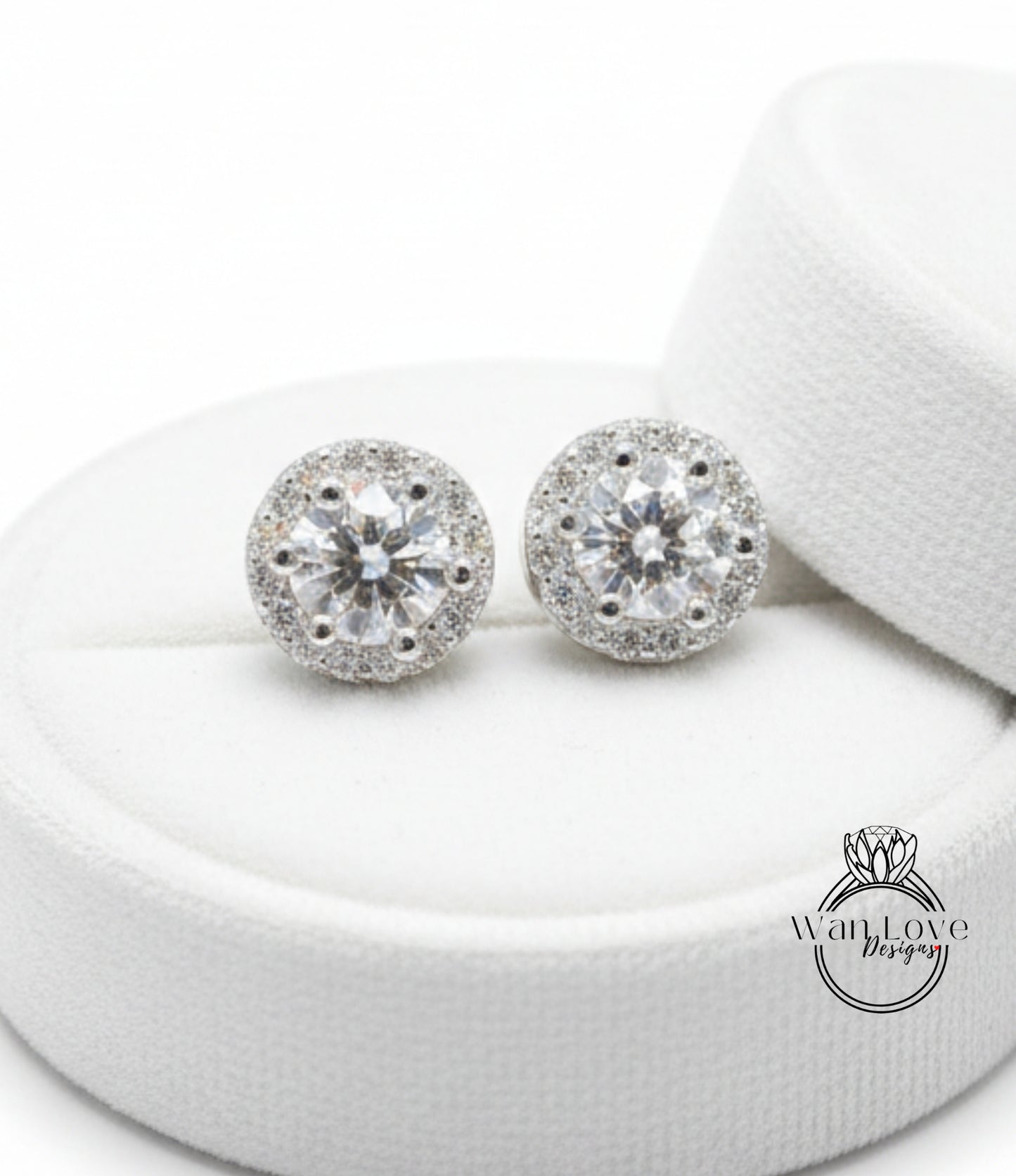 A pair of elegant diamond earrings with a large central diamond surrounded by smaller diamonds, displayed on a white circular stand.