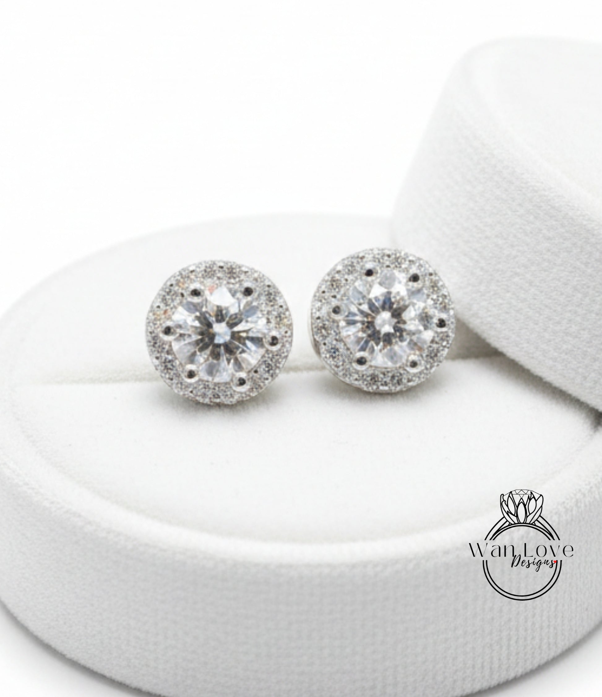 A pair of elegant diamond earrings with a large central diamond surrounded by smaller diamonds, displayed on a white circular stand.