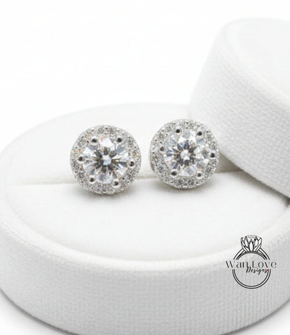 A pair of elegant diamond earrings with a large central diamond surrounded by smaller diamonds, displayed on a white circular stand.