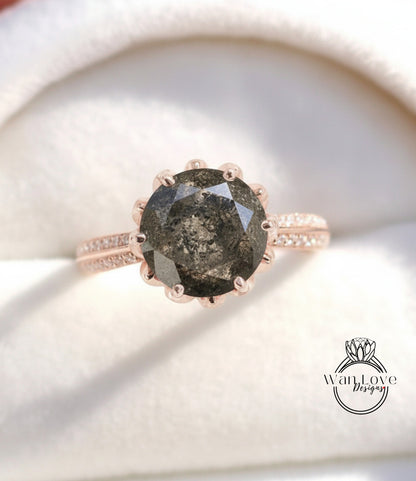 A close-up image of a rose gold ring with a large, dark grey diamond as the centerpiece, set in a white velvet background.