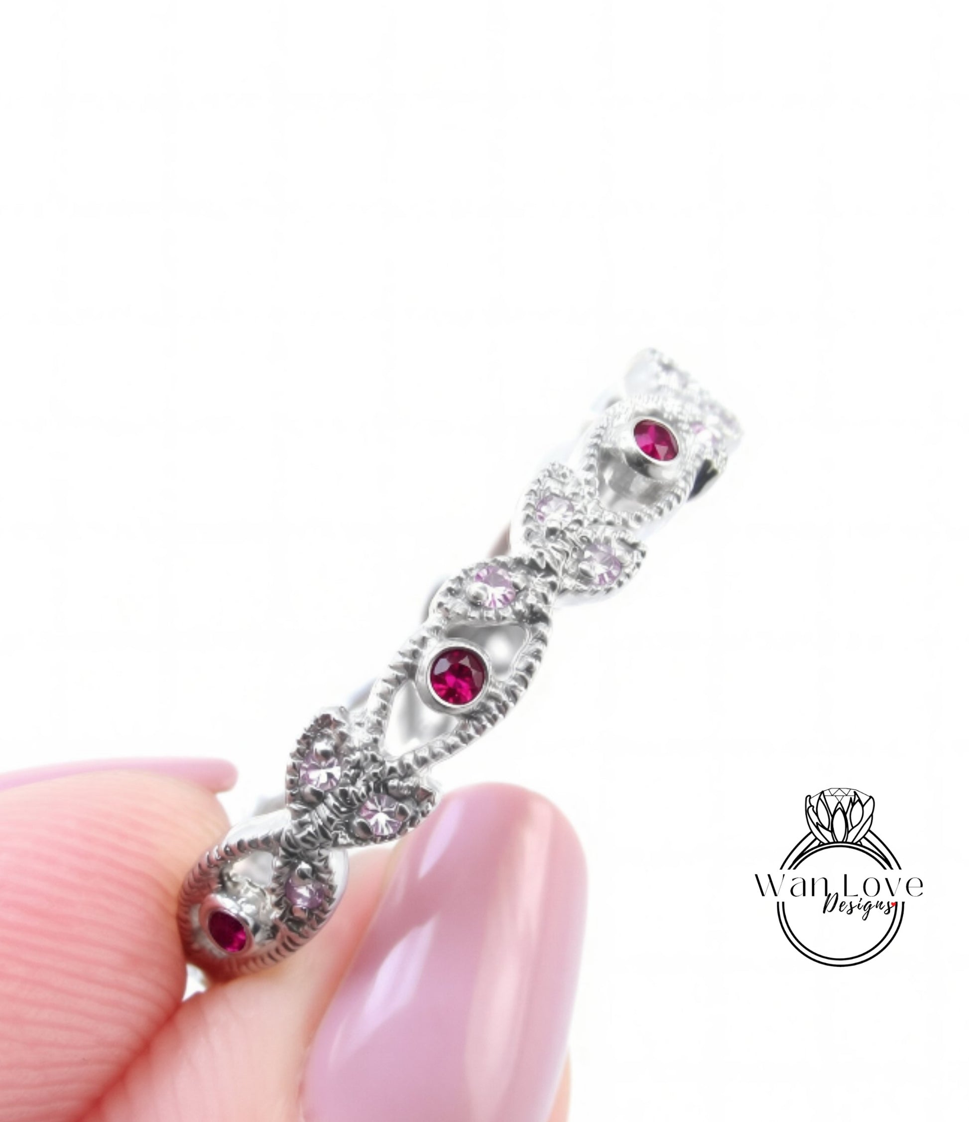 A close-up view of a person's hand holding a silver ring adorned with red gemstones.