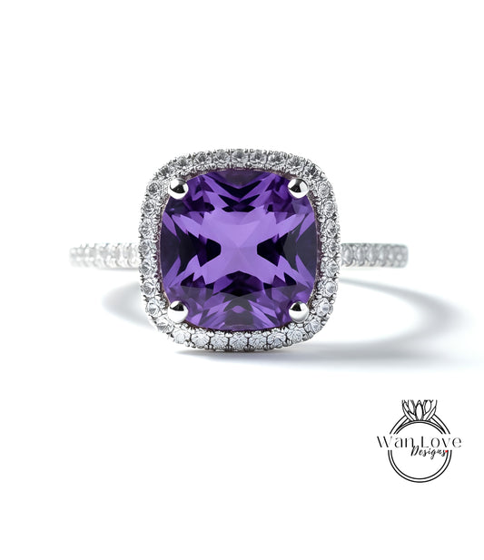 A stunning ring featuring a large, deep purple gemstone set in a halo of smaller diamonds, with a silver band and a logo for "WanLove Designs" in the bottom right corner.