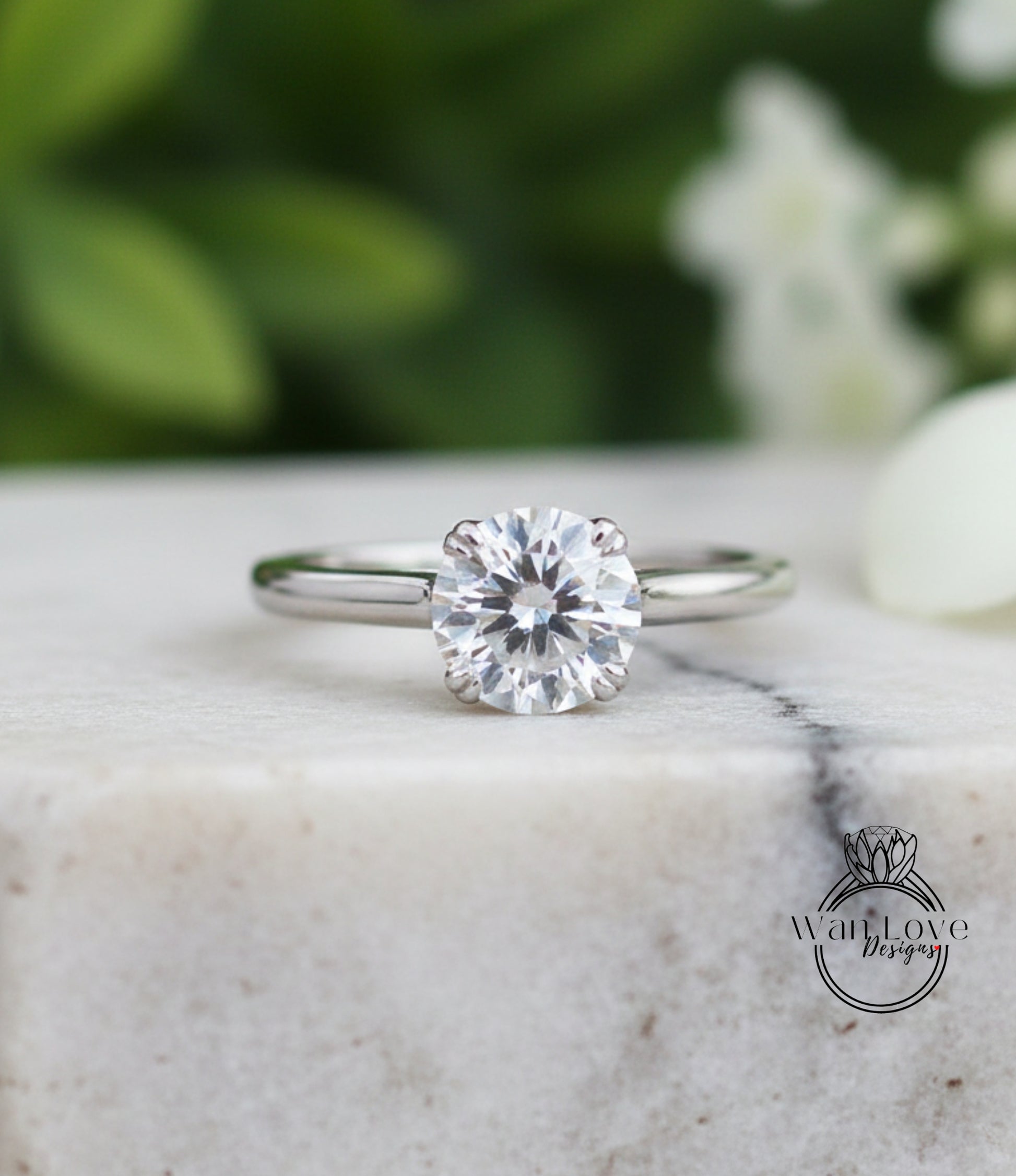 A close-up of a diamond engagement ring with a large, round diamond set in a silver band, placed on a marble surface.