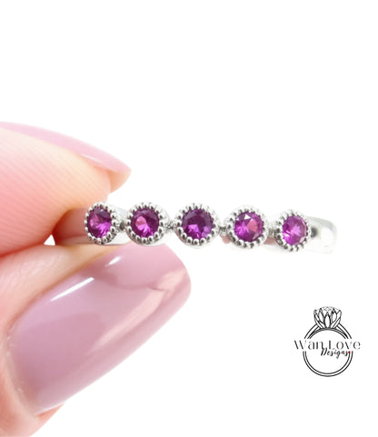 A close-up image of a person's hand holding a ring with a row of purple gemstones.