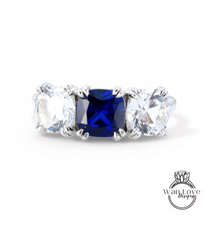 A silver ring with three large diamonds, one blue and two clear, set in a three-prong design.