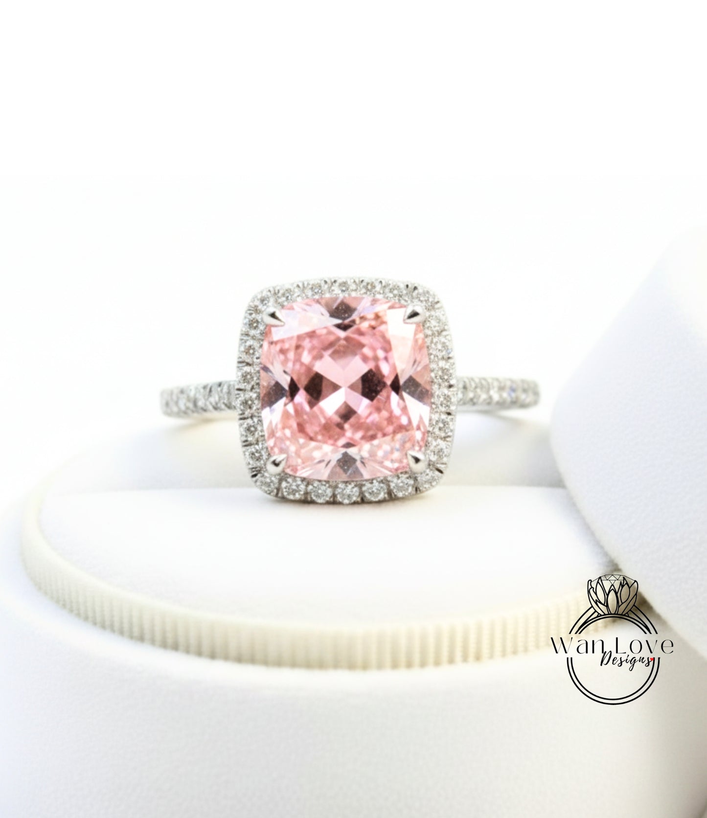 A pink gemstone ring with a halo of diamonds, displayed on a white surface.