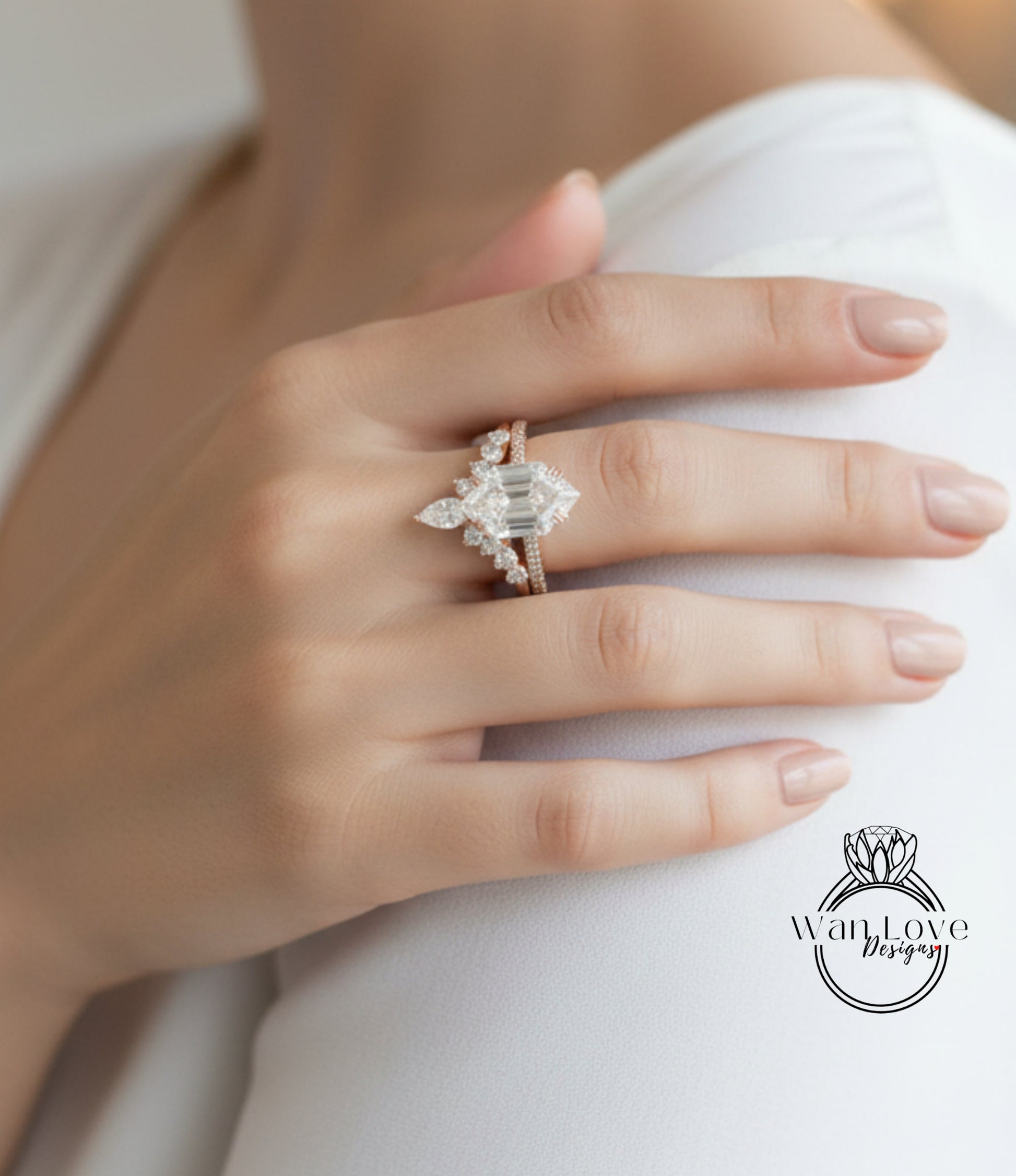 A close-up of a person's hand wearing a diamond engagement ring, with a logo for WanLove Designs visible in the background.