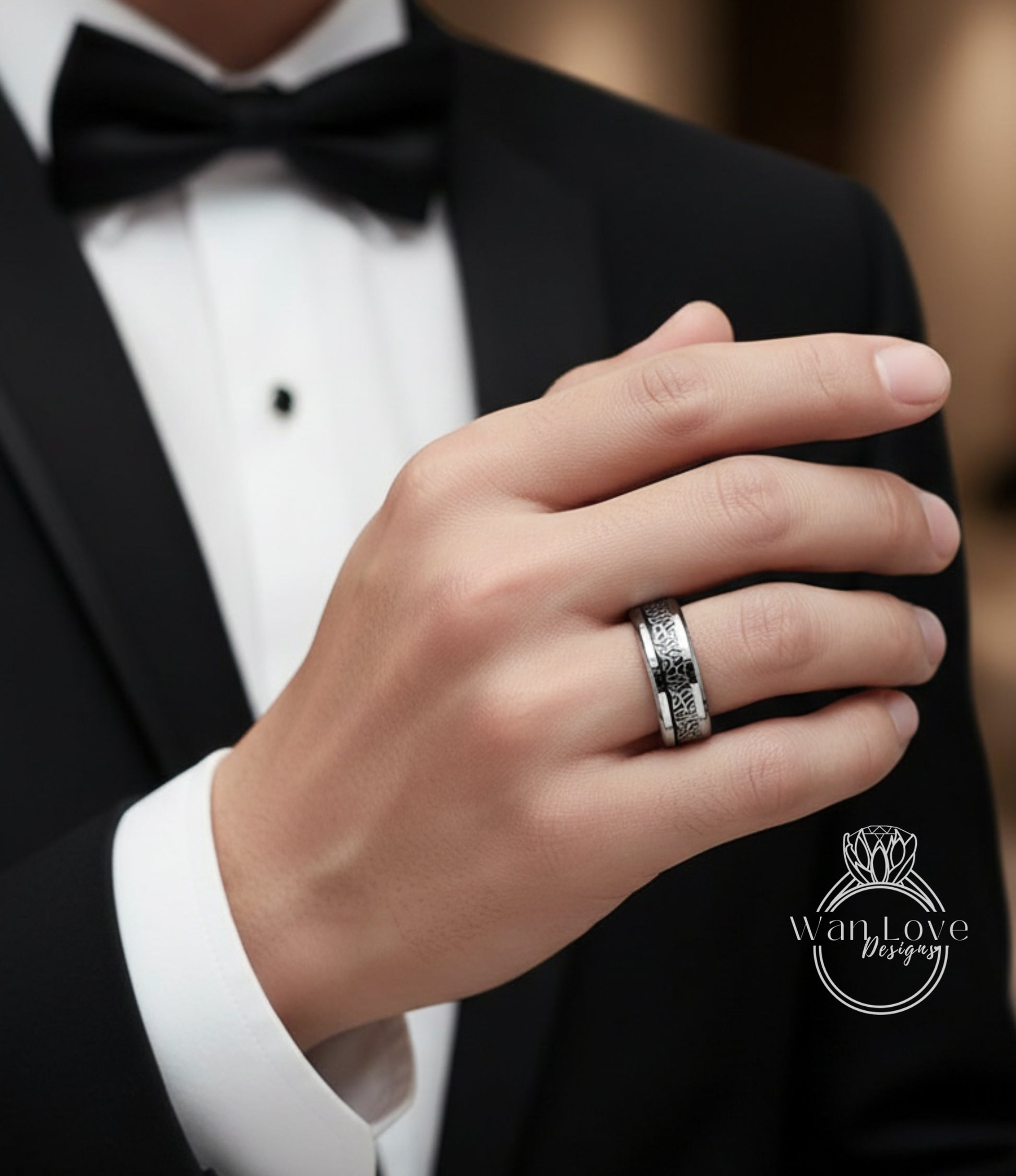 A close-up of a person's hand wearing a silver ring, with a black bow tie and a white shirt visible.