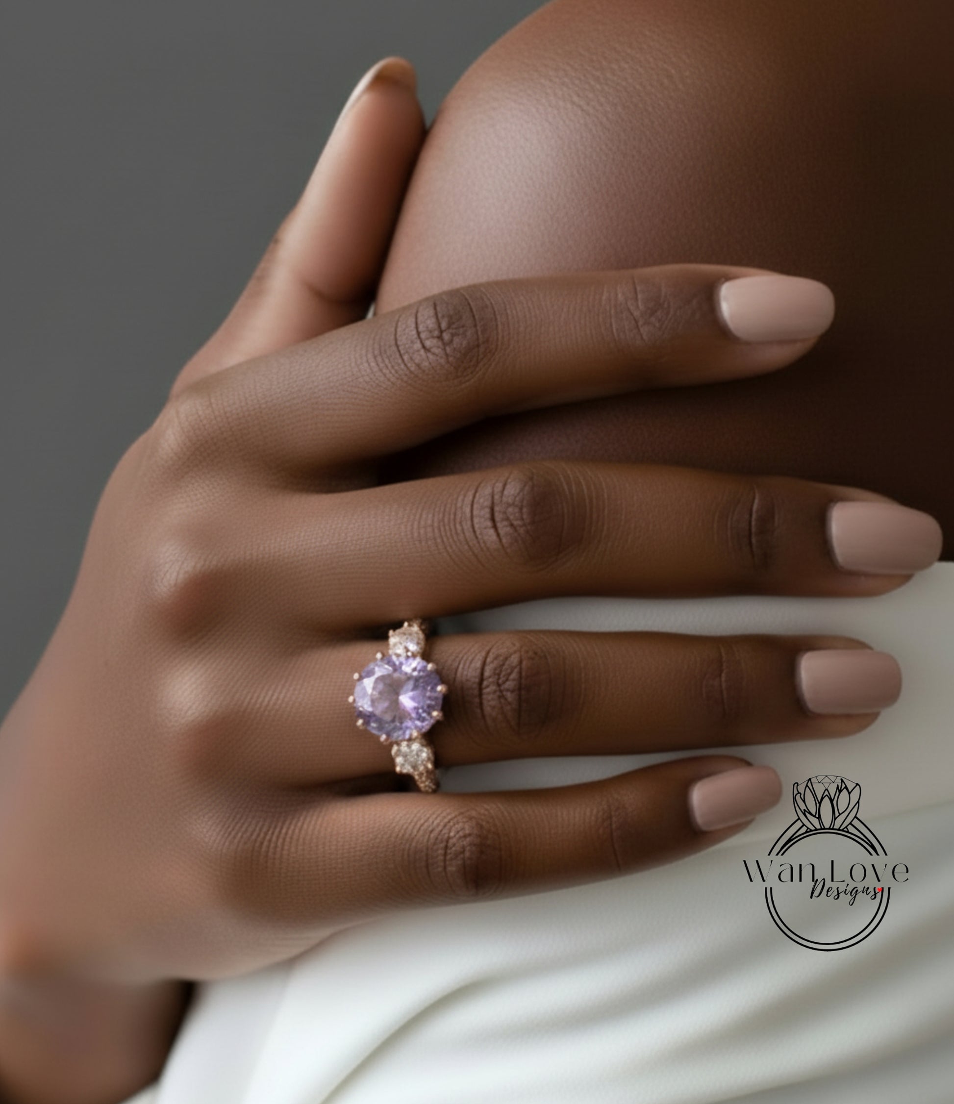 A close-up of a hand wearing a gold ring with a large purple gemstone, resting on a white fabric.