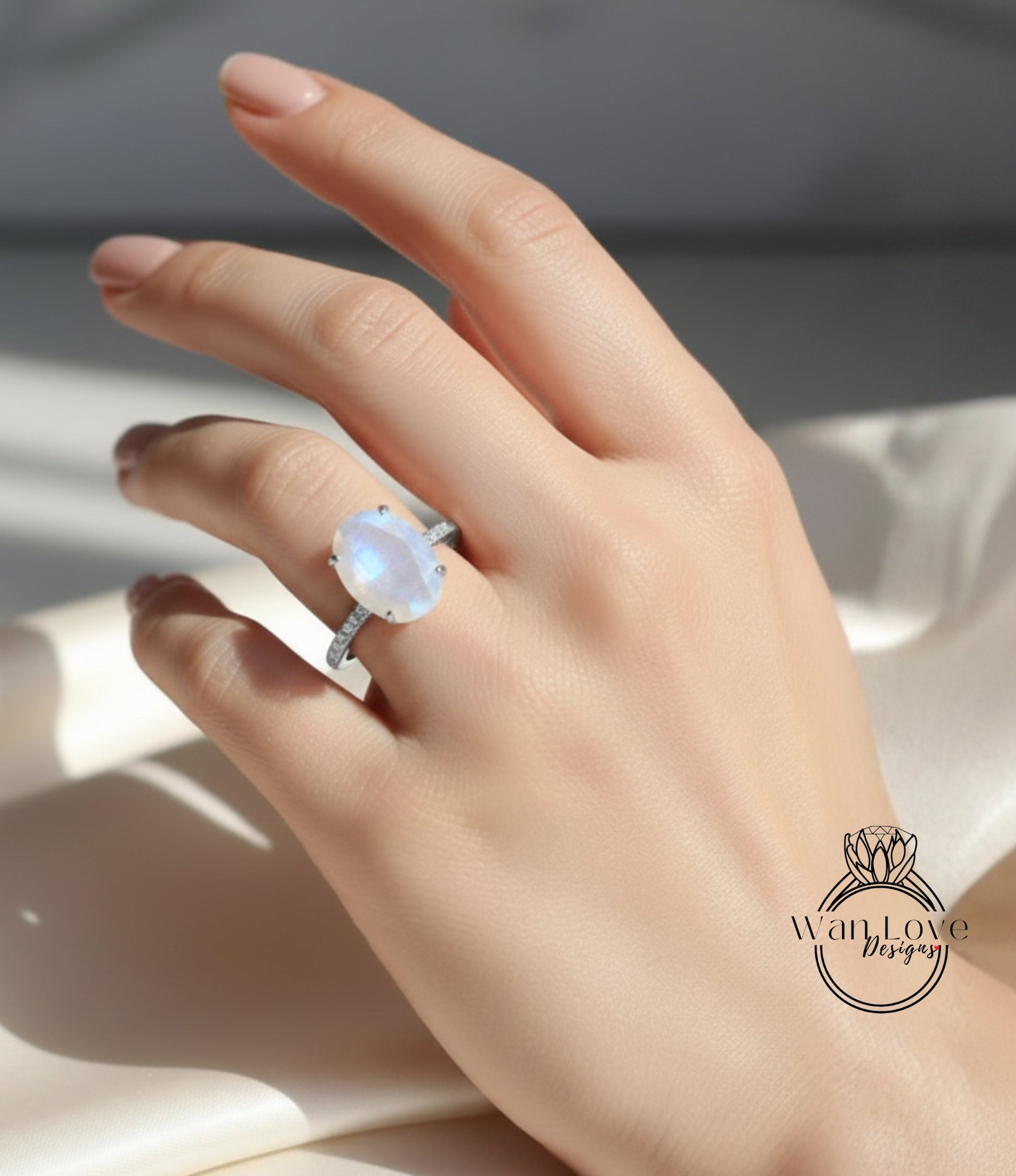 A close-up of a hand wearing a large oval-shaped ring with a moonstone, set in a silver band.