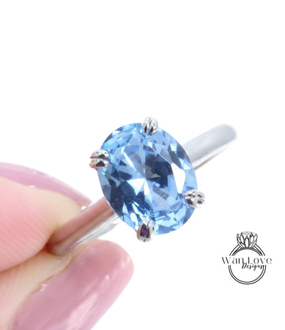A close-up image of a person's hand holding a ring with a large, clear blue gemstone.