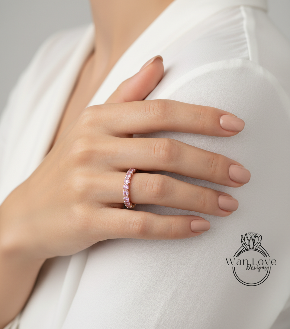 A close-up of a person's hand wearing a pink diamond ring on the ring finger.