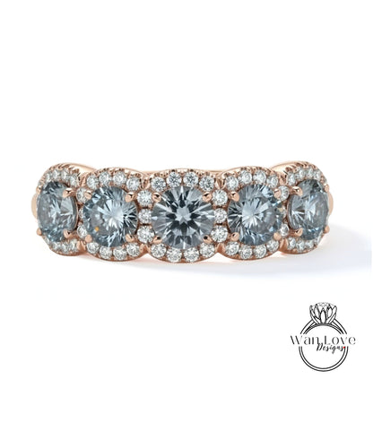 A ring with a row of four large, clear gemstones set in a halo of smaller diamonds, all set in a rose gold band.