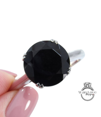 A close-up image of a person's hand holding a large, black gemstone ring with a silver band.