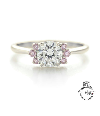 A close-up of a diamond engagement ring with a large central diamond surrounded by smaller diamonds and pink gemstones.