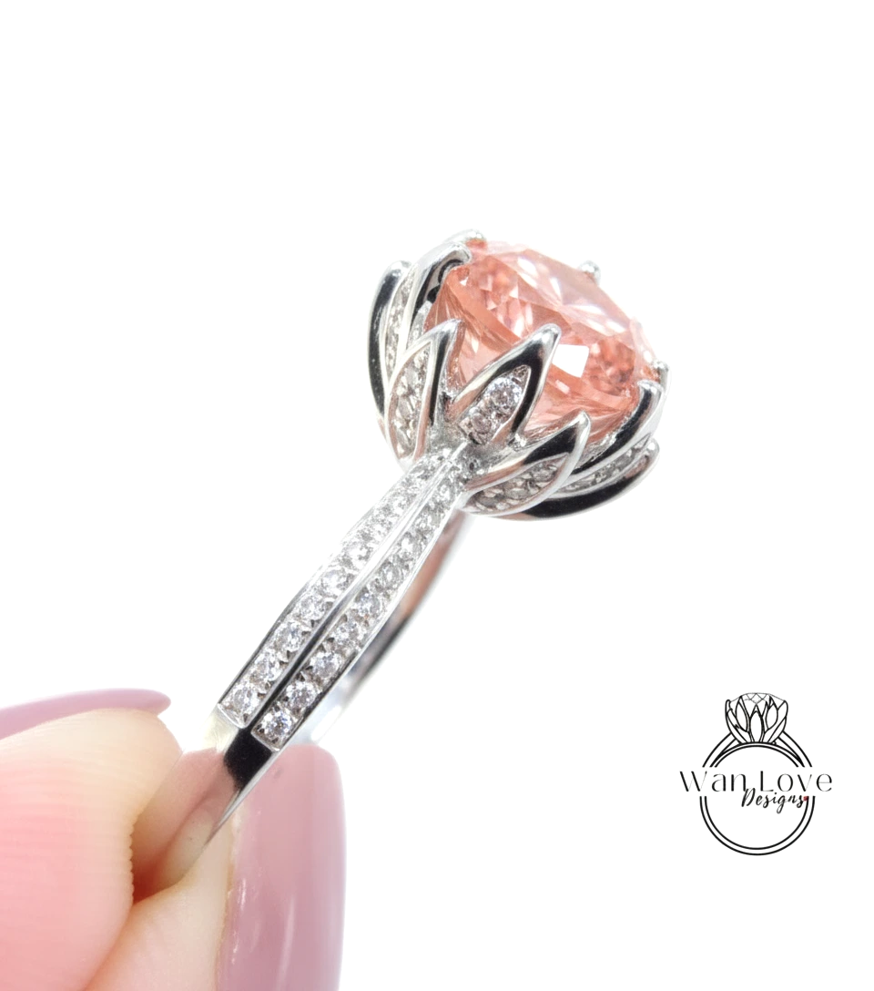 A close-up of a person's hand holding a silver ring with a large, round, pink gemstone.