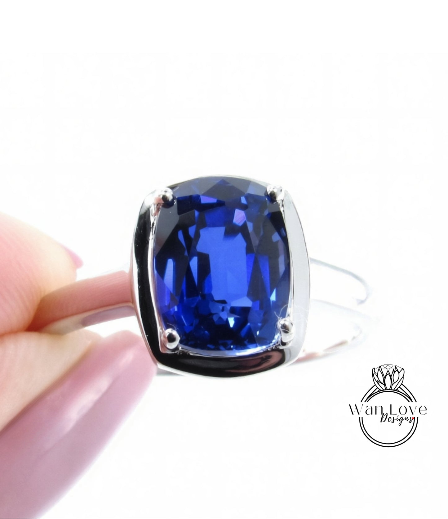 A hand holding a silver ring with a large blue gemstone, likely a sapphire or blue topaz.