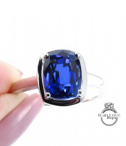 A hand holding a silver ring with a large blue gemstone, likely a sapphire or blue topaz.