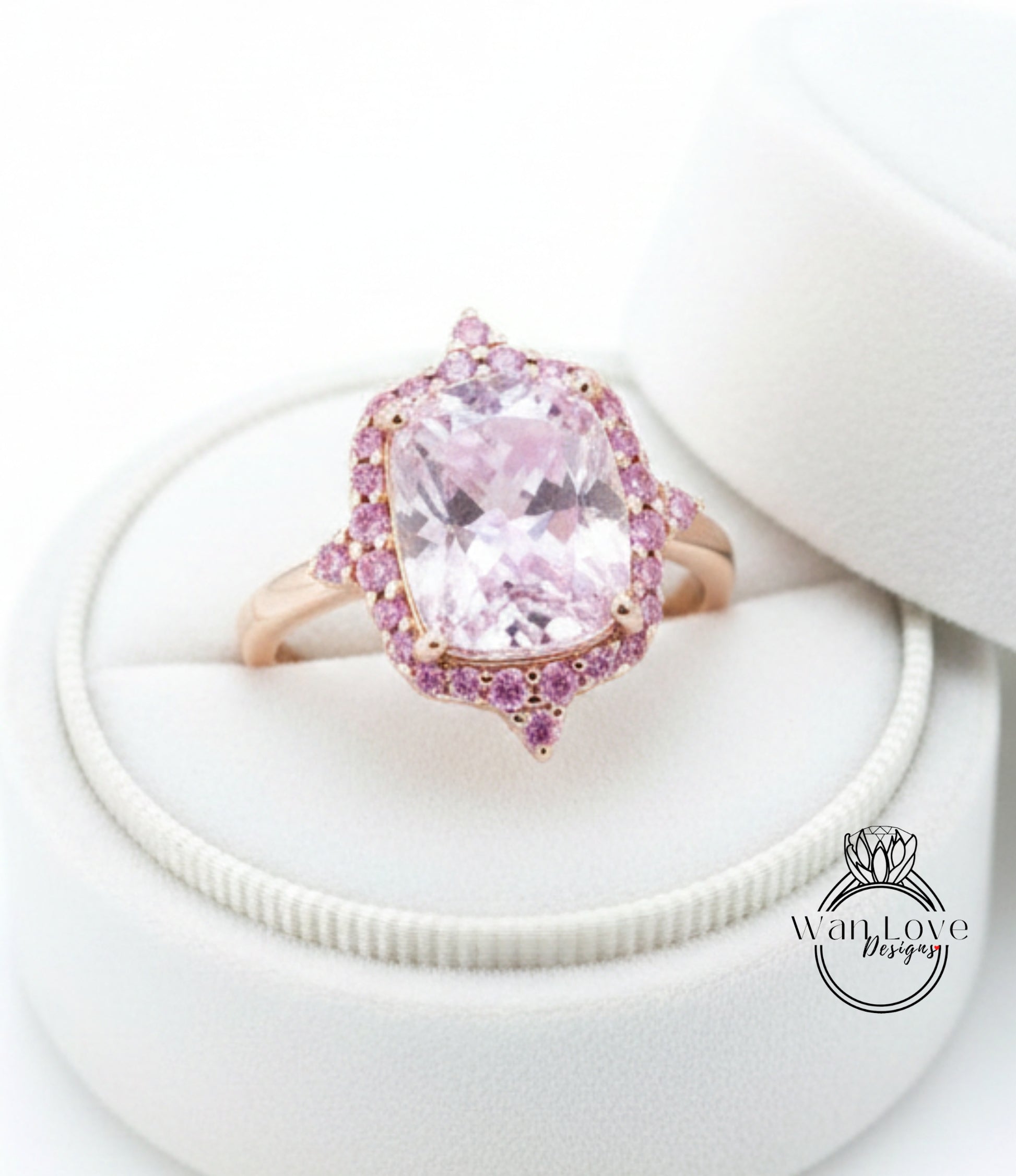 A pink gemstone ring with a large central stone surrounded by smaller stones, displayed in a white jewelry box.