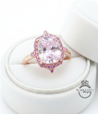 A pink gemstone ring with a large central stone surrounded by smaller stones, displayed in a white jewelry box.