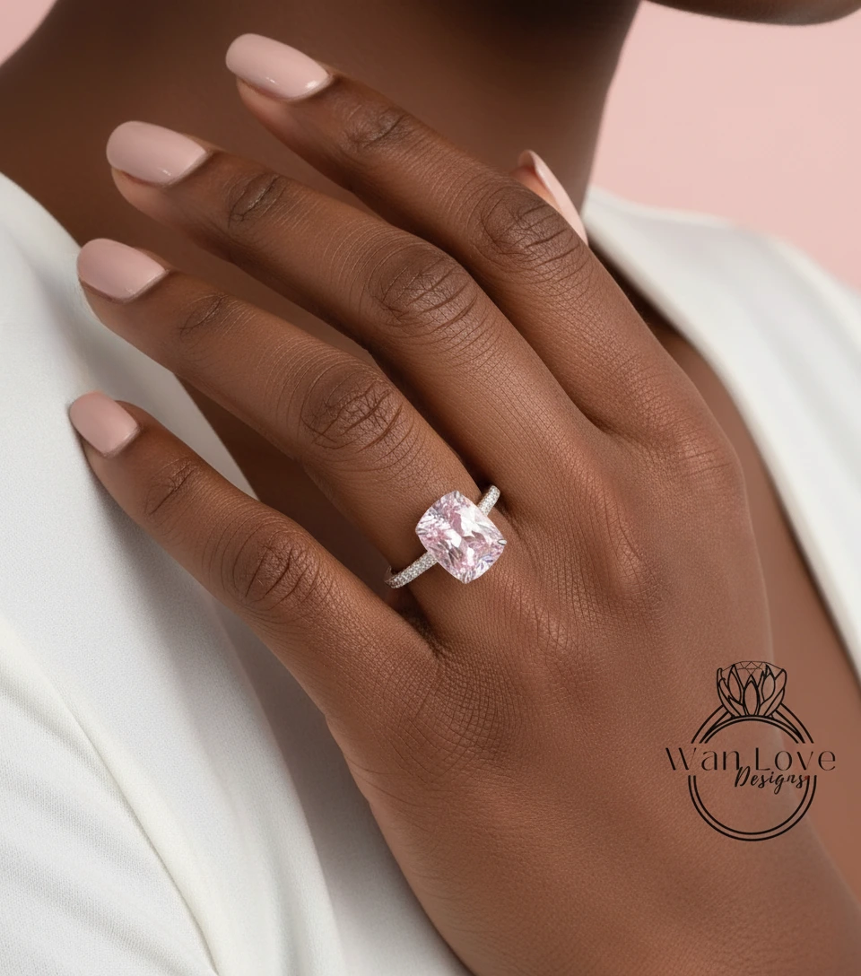 A close-up of a person's hand wearing a large, pink diamond engagement ring.