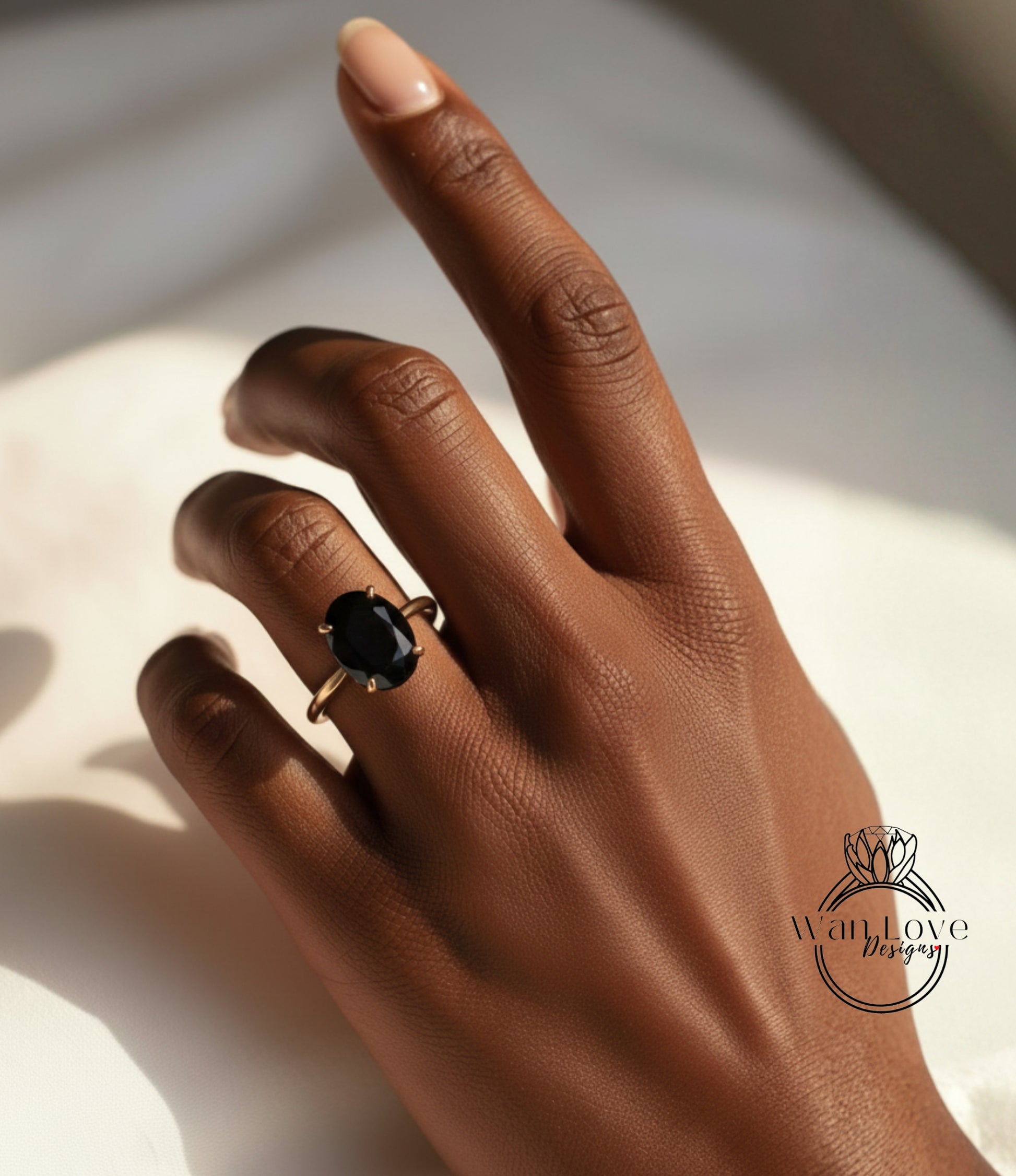 A close-up of a hand wearing a gold ring with a large black gemstone, resting on a white surface.