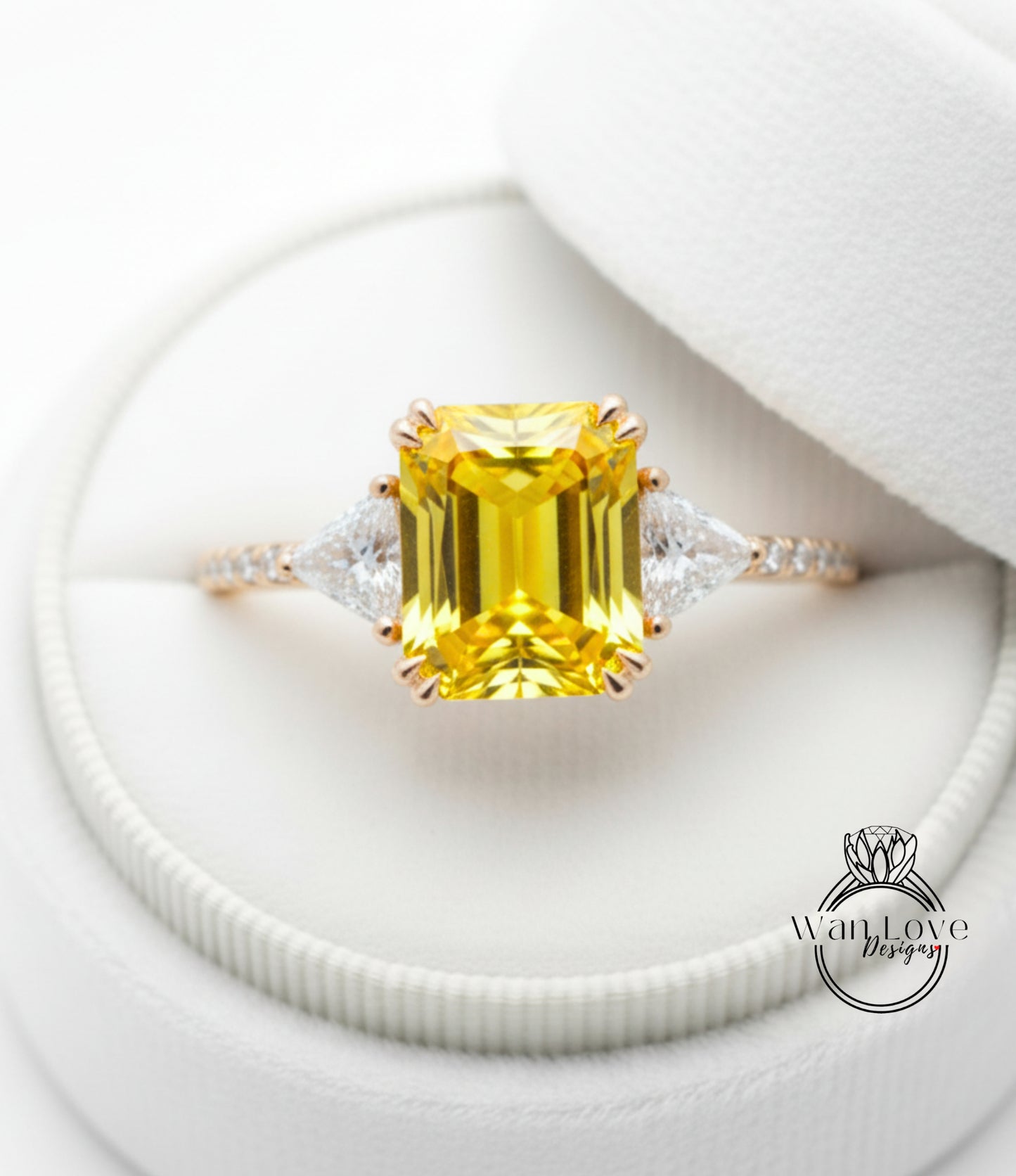 A yellow diamond engagement ring with a large central diamond and smaller diamonds on either side, displayed in a white jewelry box.