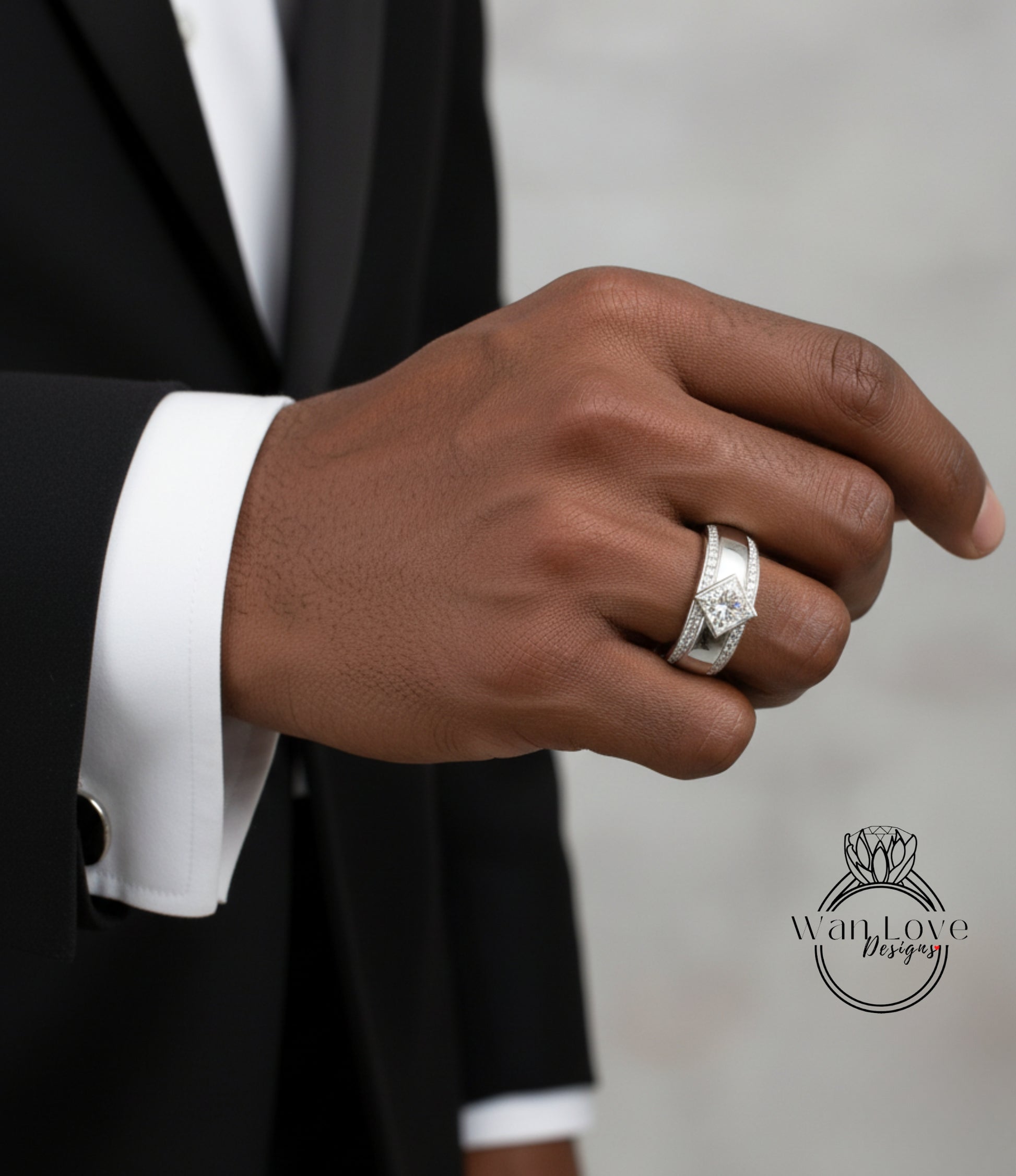 A close-up of a person's hand wearing a diamond ring, with a black suit jacket visible.