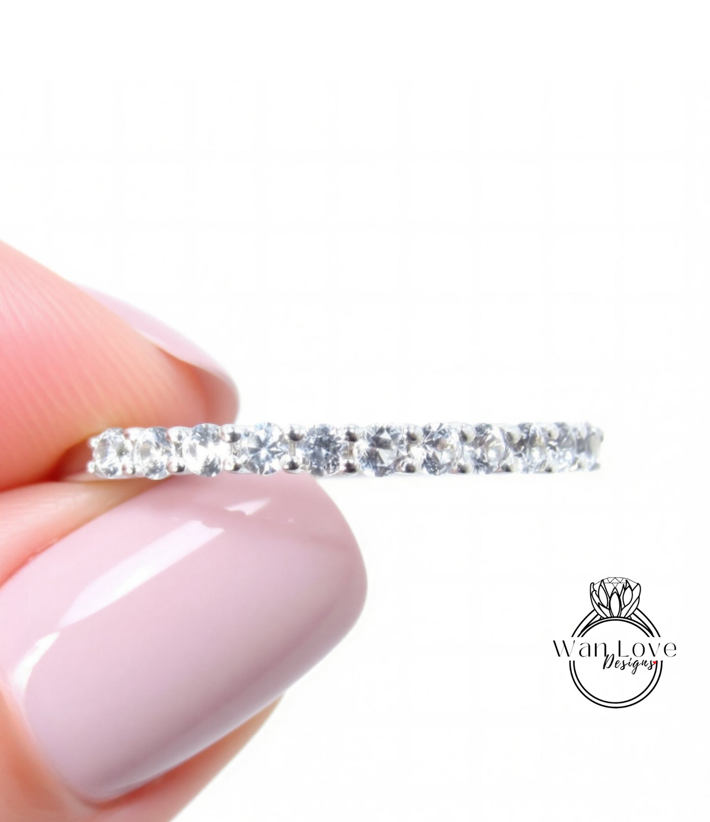 A close-up image of a person's hand holding a ring with a row of clear gemstones.