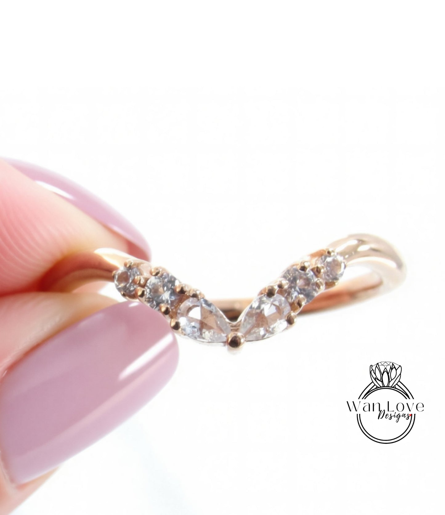 A close-up image of a person's hand holding a gold ring with a v-shaped band and small diamonds.