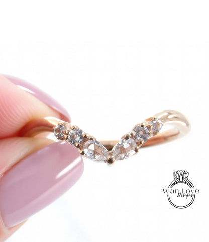 A close-up image of a person's hand holding a gold ring with a v-shaped band and small diamonds.