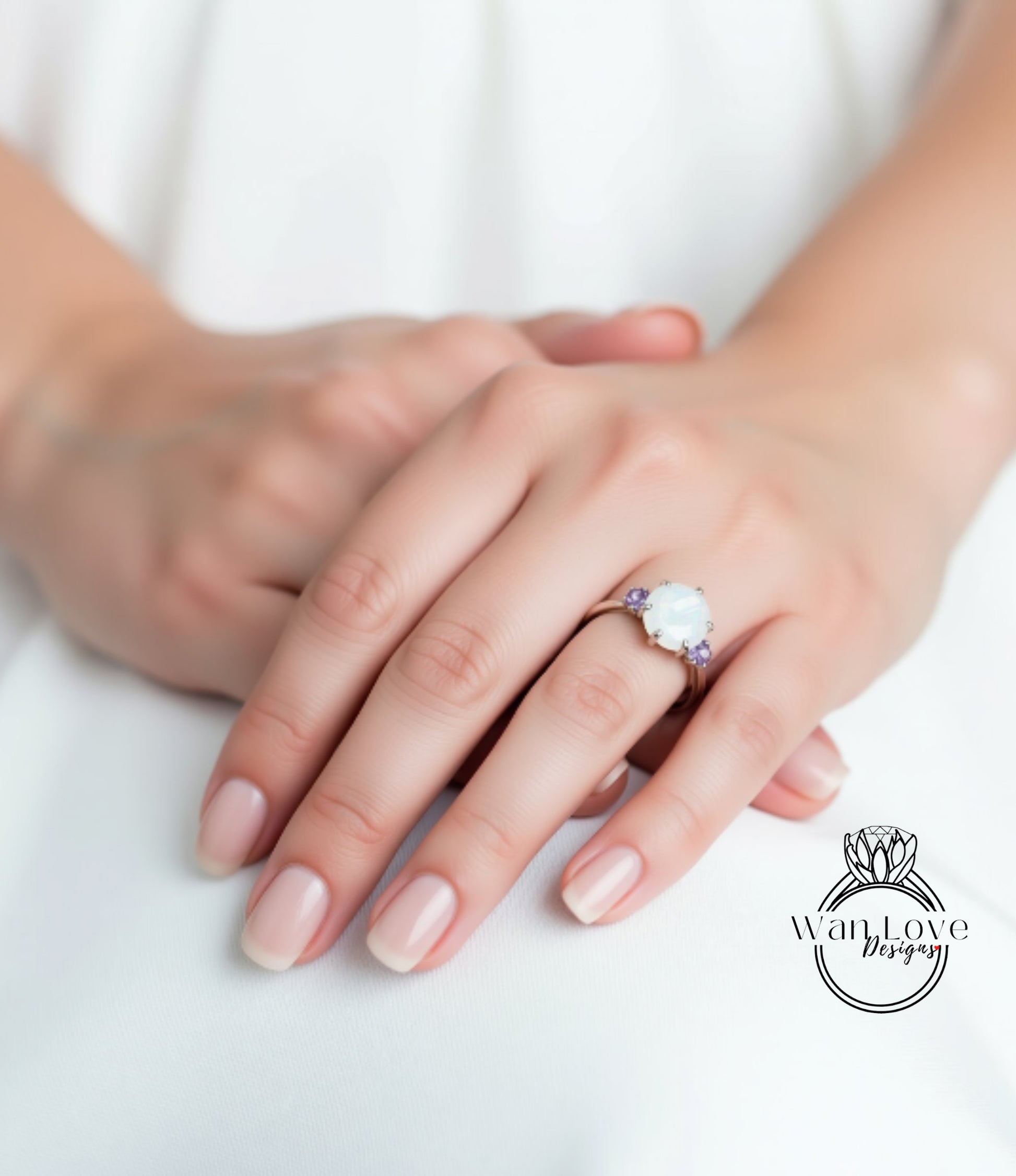 A close-up of a person's hands wearing a ring with a large white stone, resting on a white surface.
