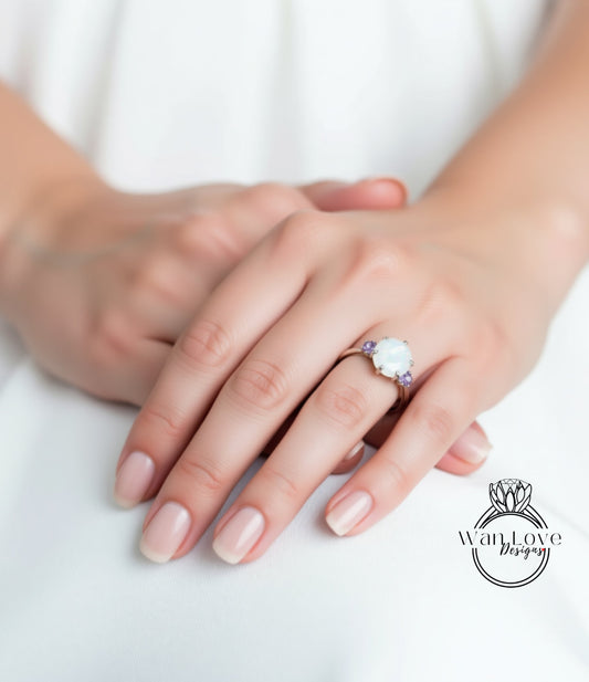 A close-up of a person's hands wearing a ring with a large white stone, resting on a white surface.